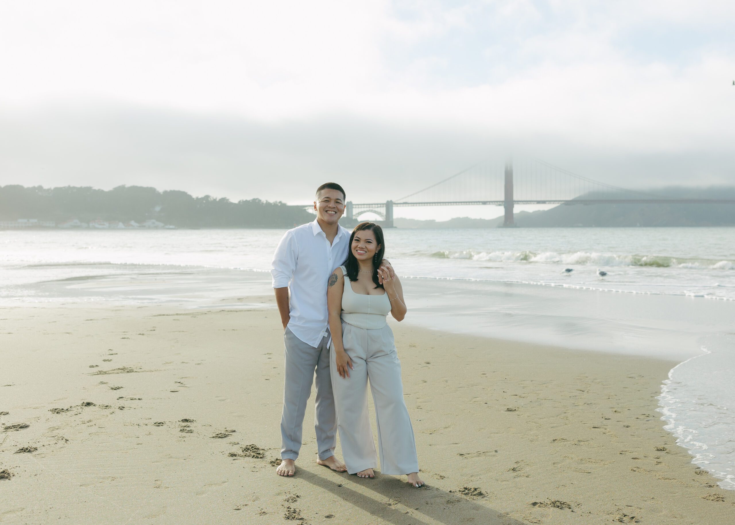 A couple taking beach engagement photos in front off the golden gate bridge