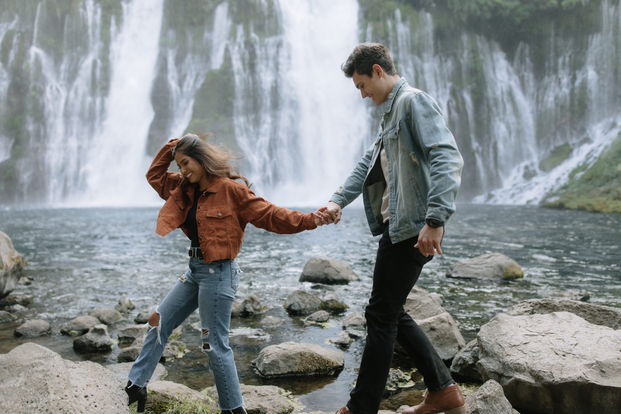 a couple holding hands while walking In front go a waterfall