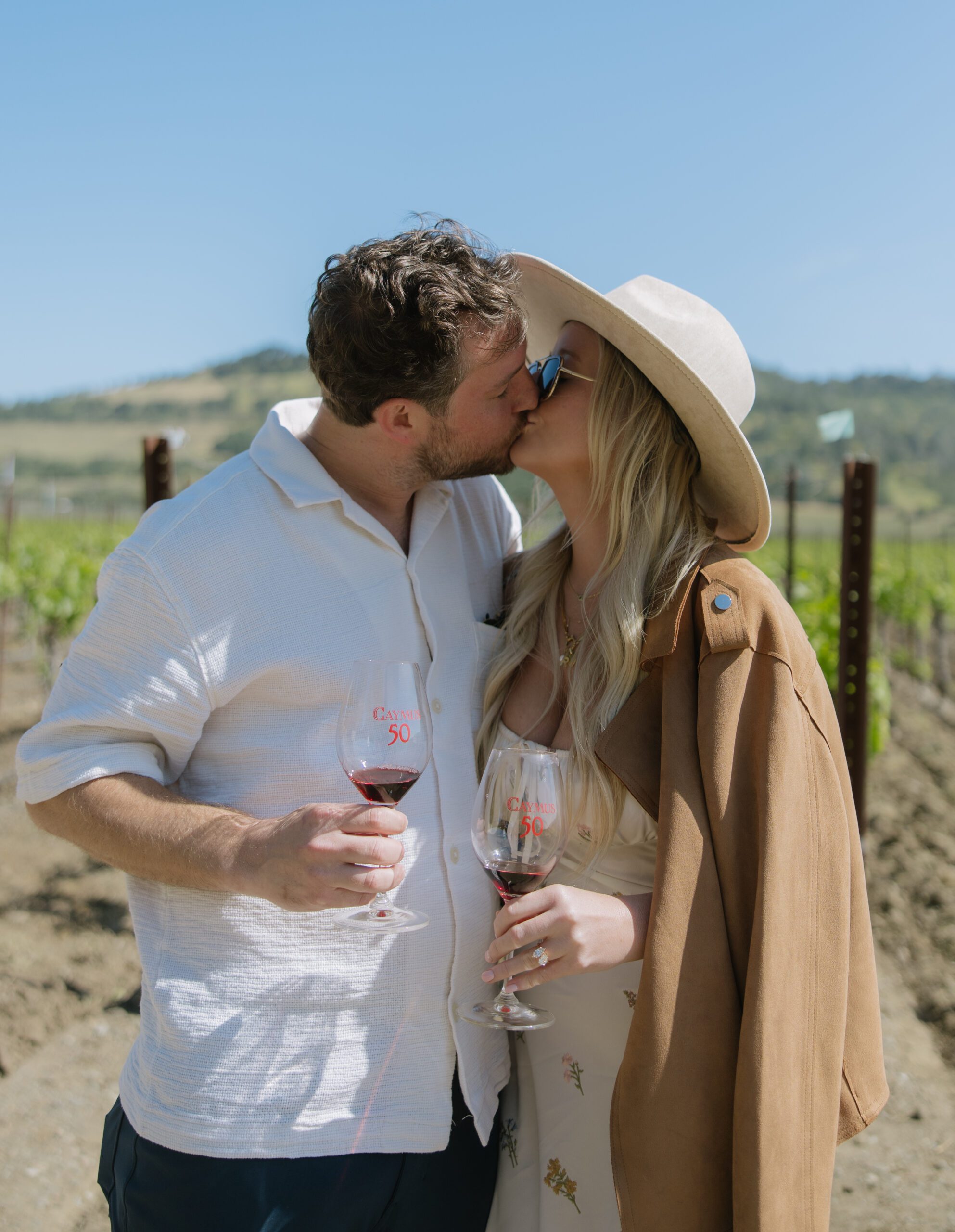 A couple holding wine glasses and kissing after getting engaged