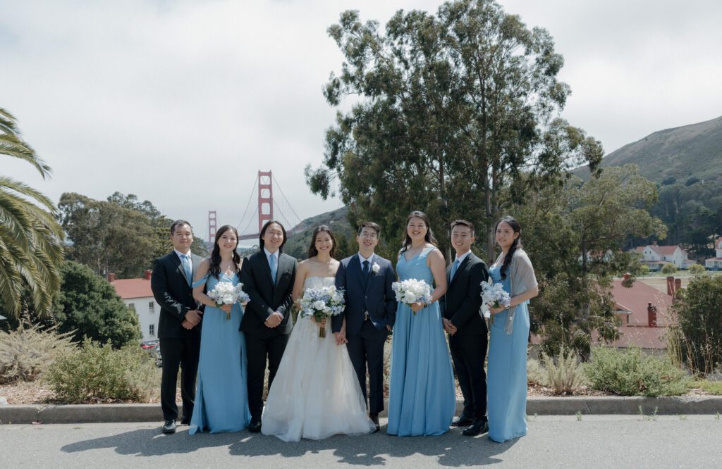 A wedding party posing for photos in front of the golden gate bridge