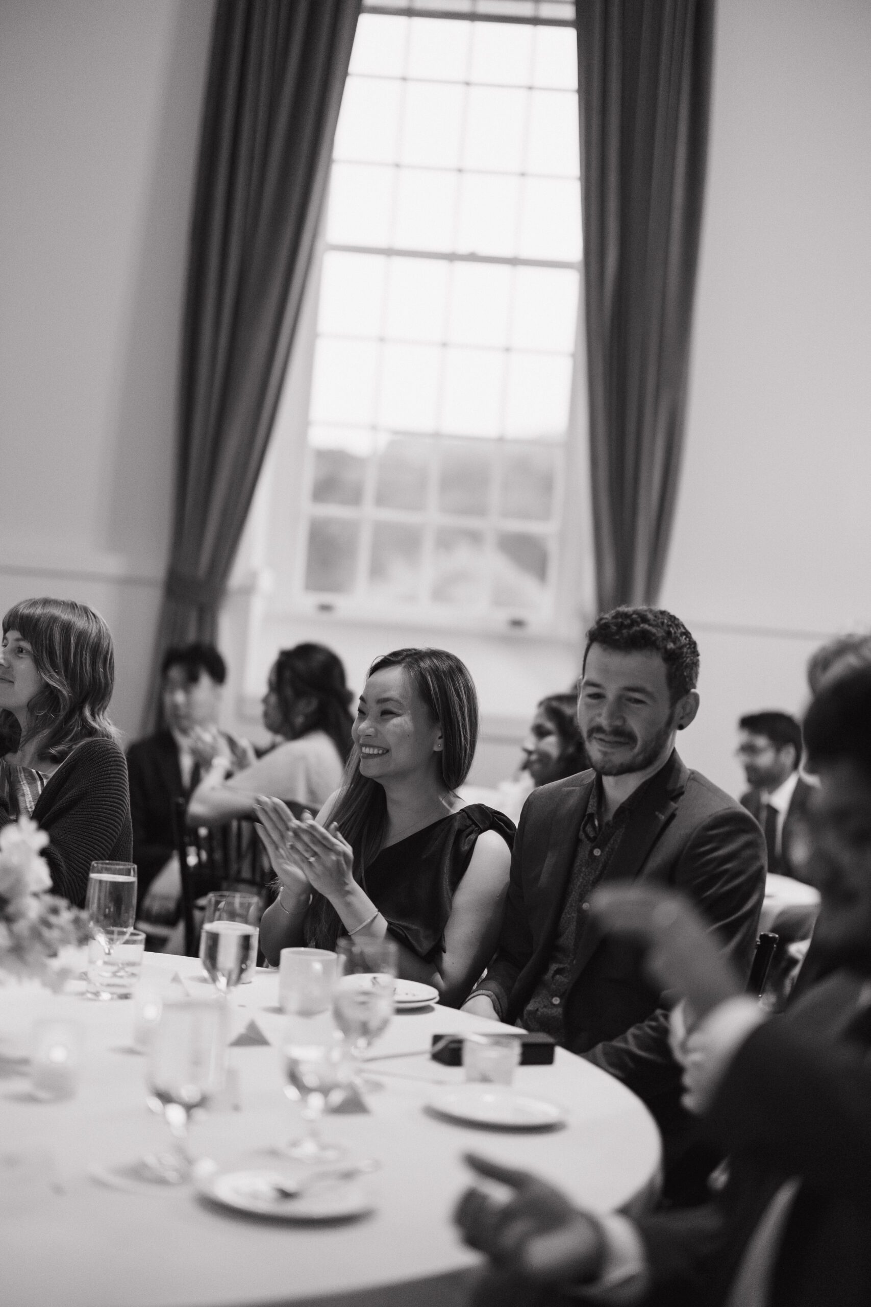 A black and white candid photo of wedding guests at a reception