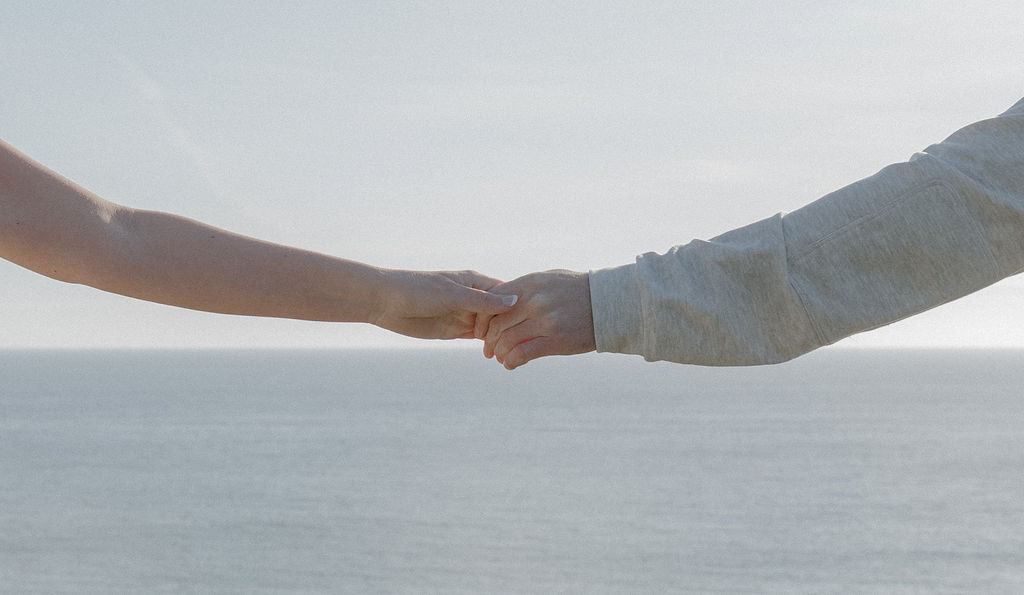 A couple reaching out to hold hands in front of the ocean