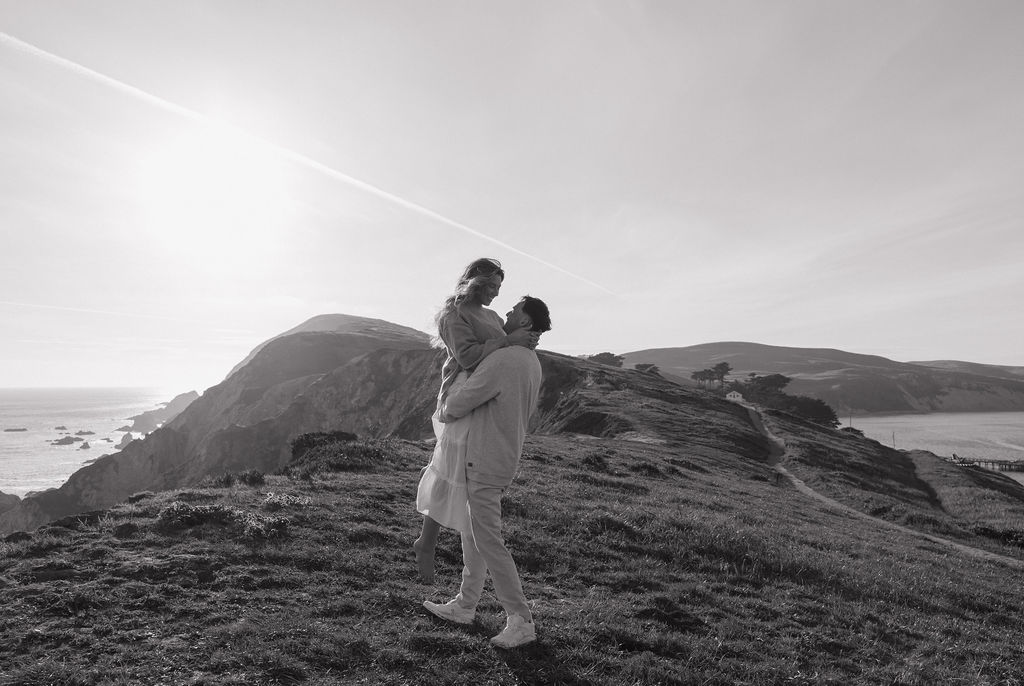 A black and white photo of a man holding his fiancee during engagement photos