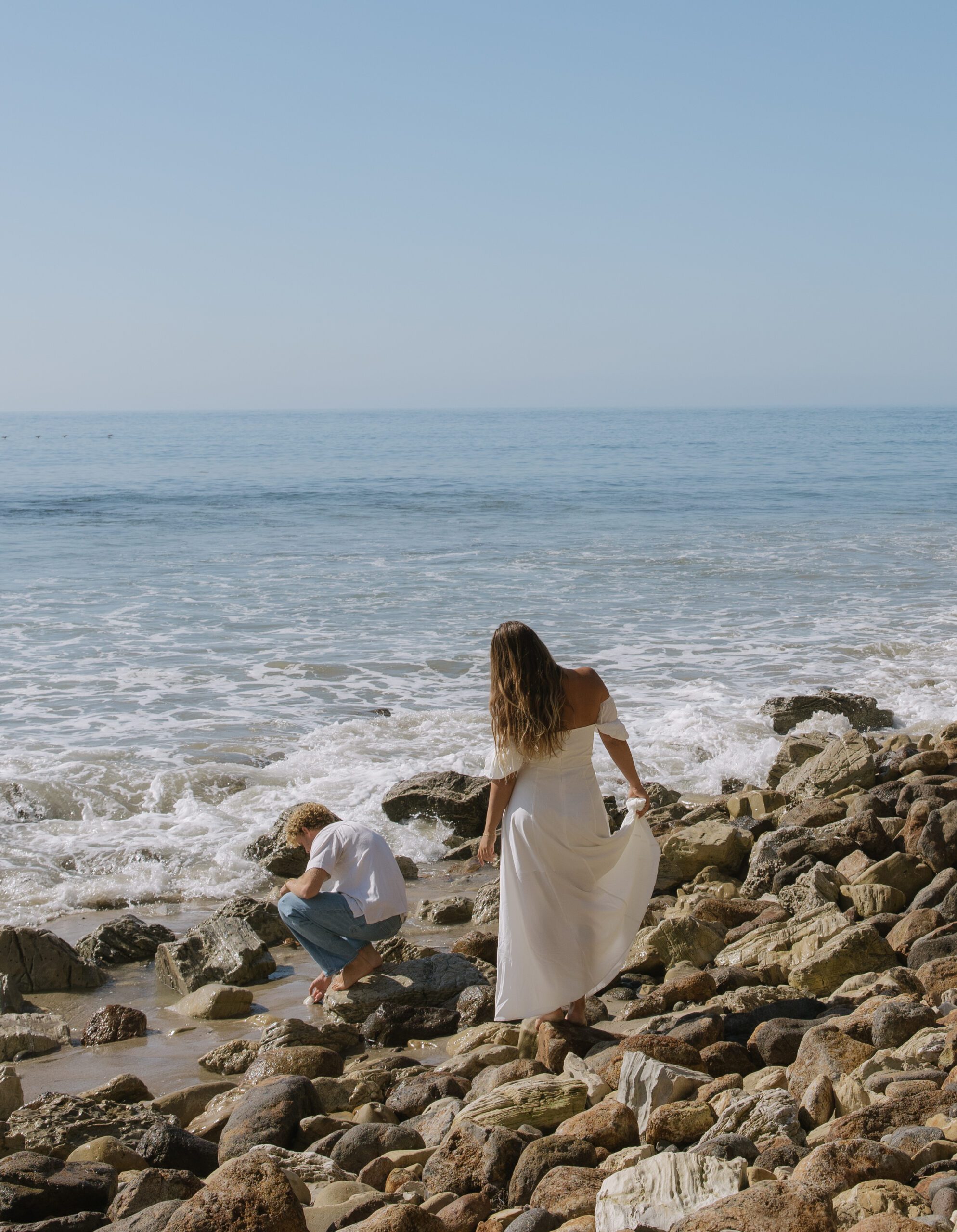 A woman standing behind her fiance for beach engagement pictures