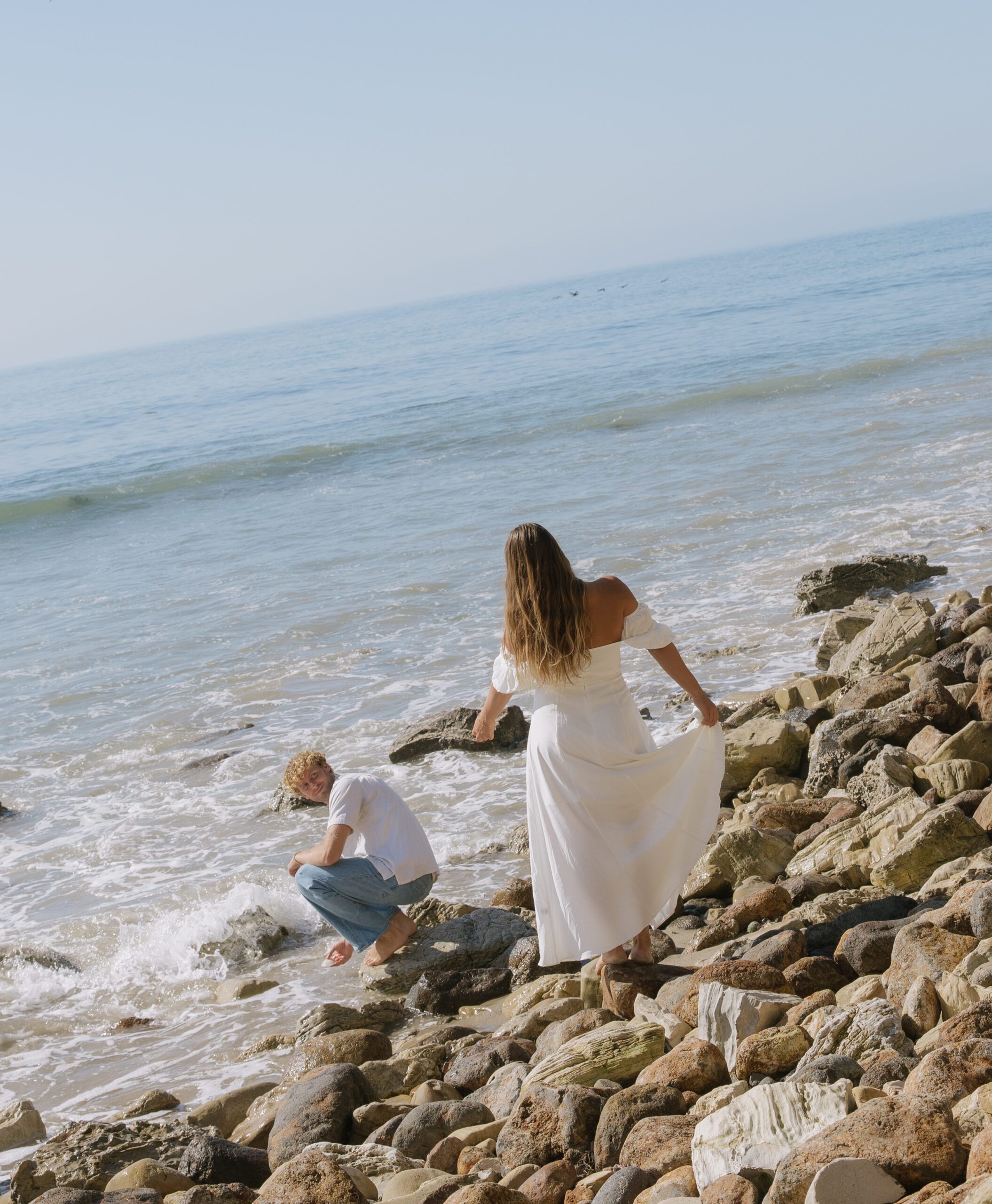 A woman standing behind her fiance for beach engagement pictures