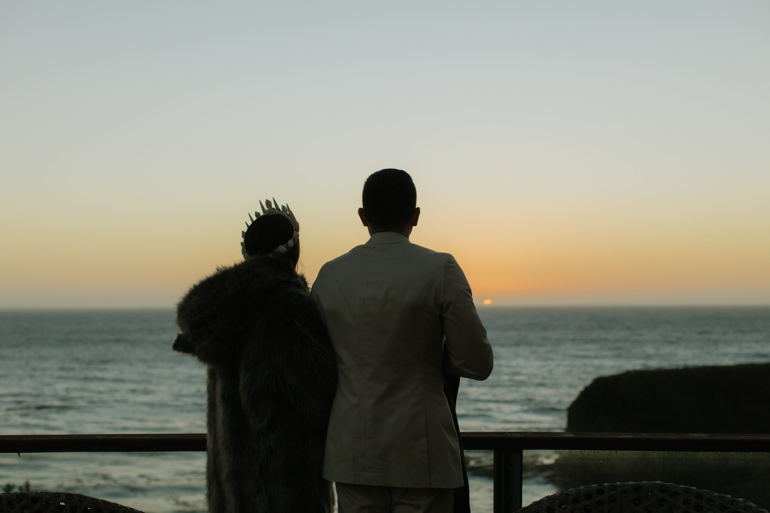 A bride and groom watching the sunset from their waterfront wedding location