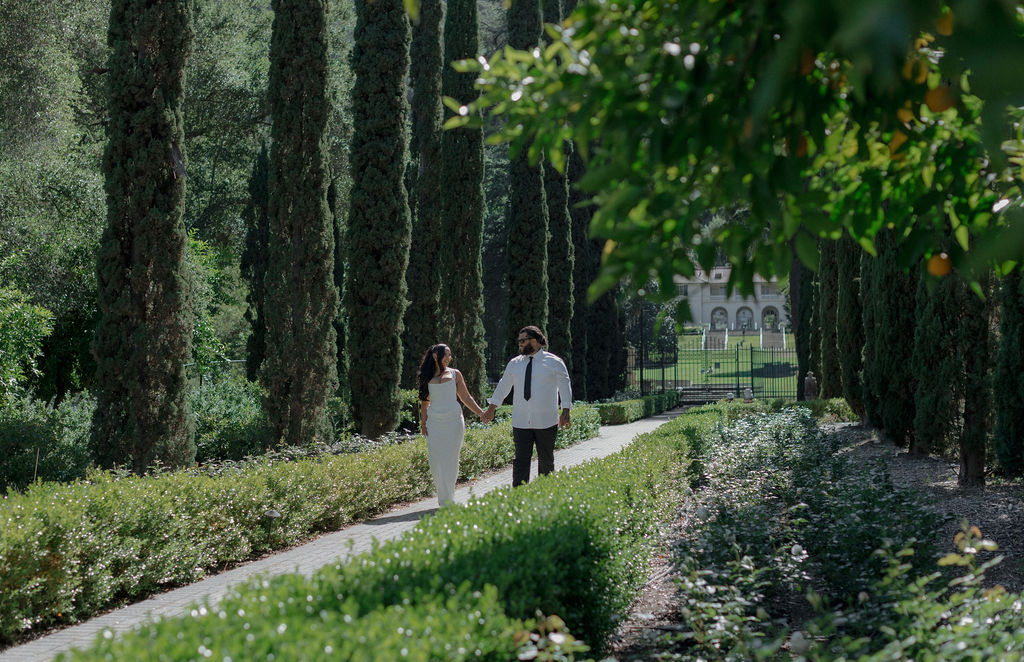 A bride and groom walking along a garden path holding hands