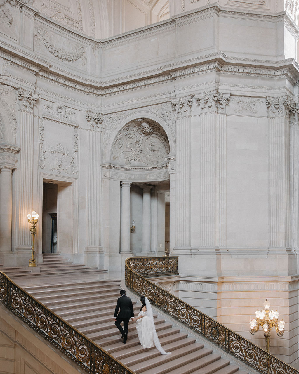 A bride and groom walking up the grand staircase in San Francisco City Hall