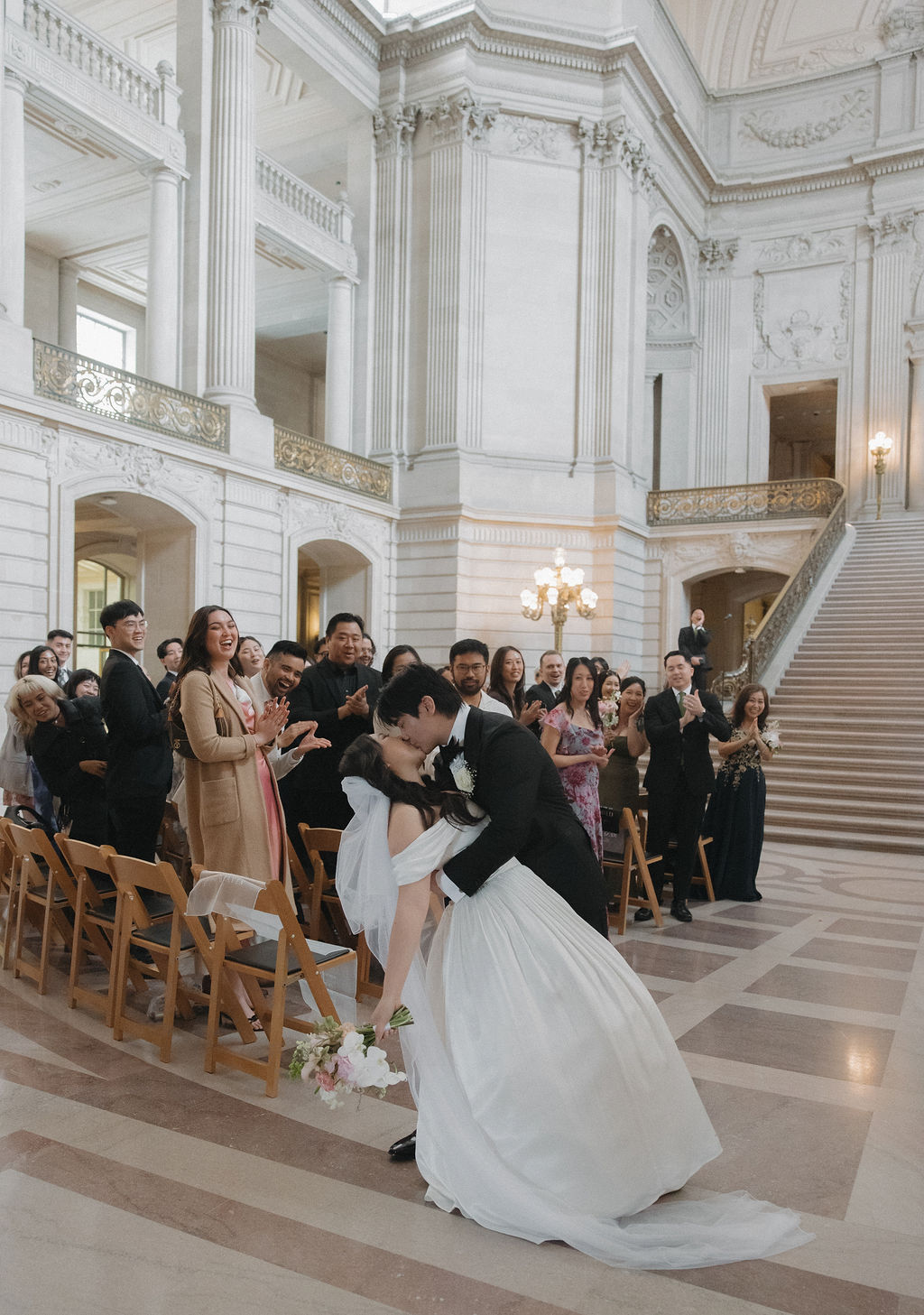 A family celebrating after a San Francisco City hall wedding while the bride and groom kiss