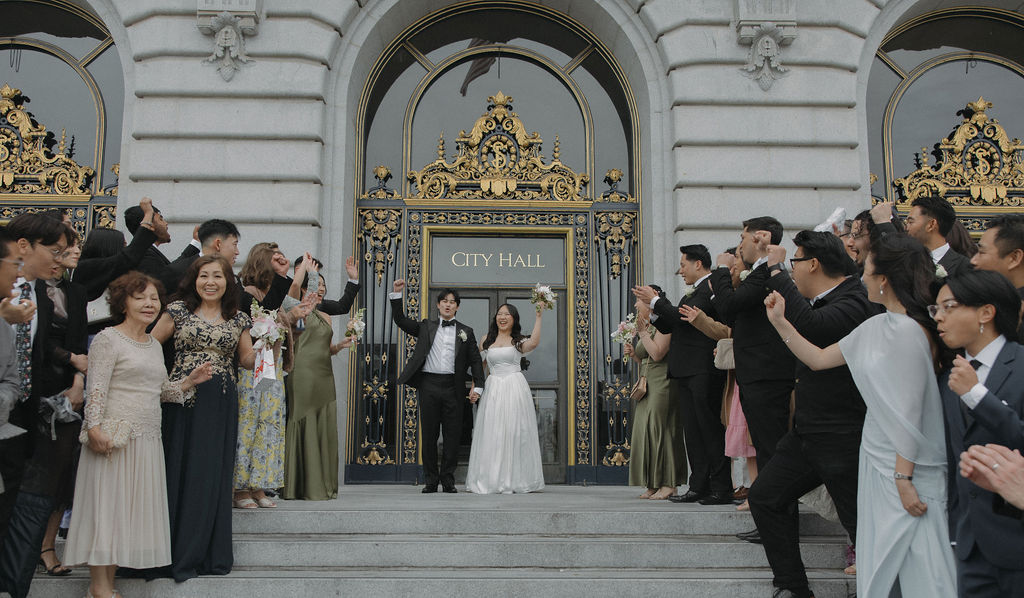 A bride and groom cheering with guests after their san francisco city hall wedding