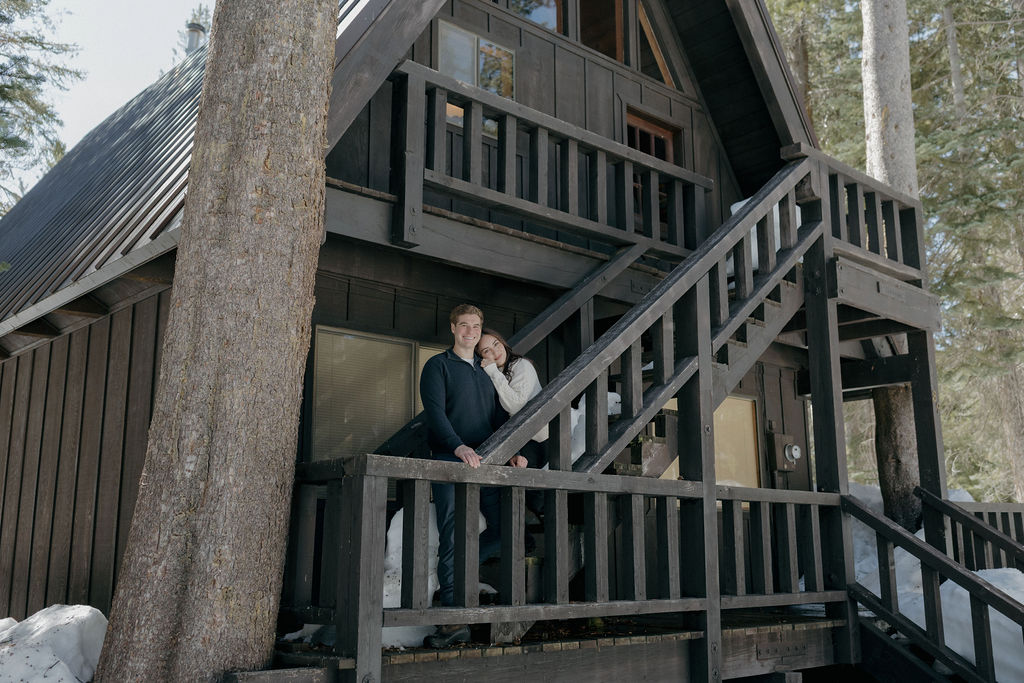 A couple posing for winter engagement photos at a cabin